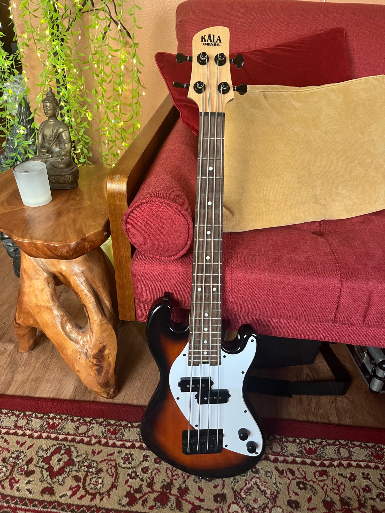 A bass beside the red sofa and cushions in Music Medicine Studio