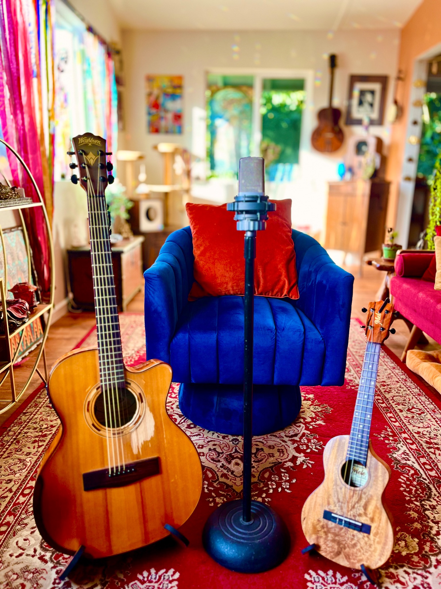 A microphone centered in front of a blue chair, with an acoustic guitar and ukulele in the bright studio